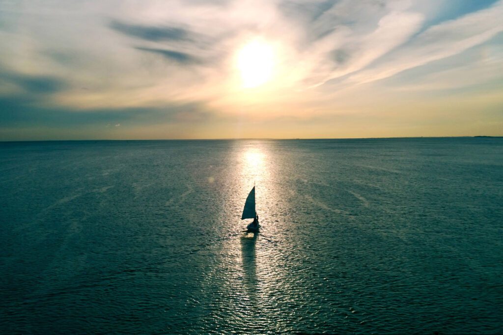 Ey Sailboat Floating On The Water Towards The Horizon In The Rays Of The Setting Sun.jpg